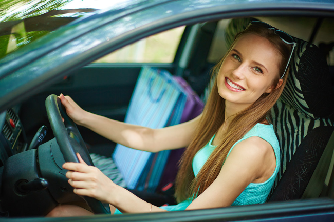 Woman sitting in a car, smiling, with a bag in the background